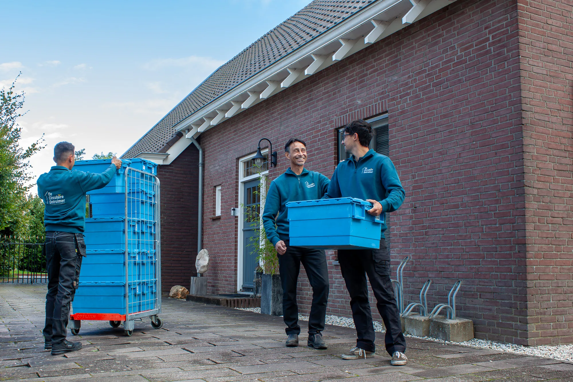 Medewerkers van De Circulaire Ontruimer dragen opbergkratten naar een verhuiskar bij een woning
