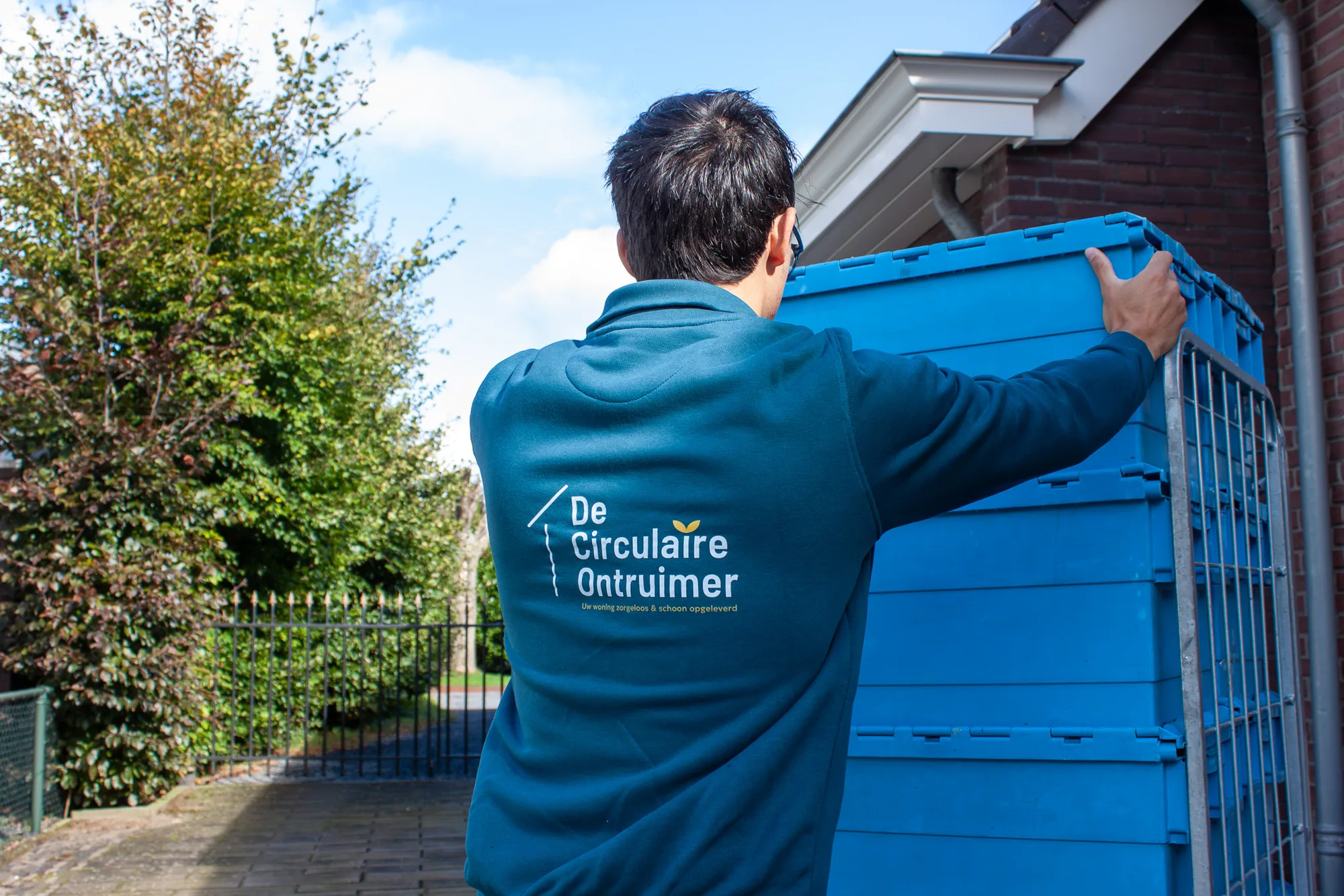 Medewerker van De Circulaire Ontruimer pakt een blauwe opbergkrat vast bij een woning