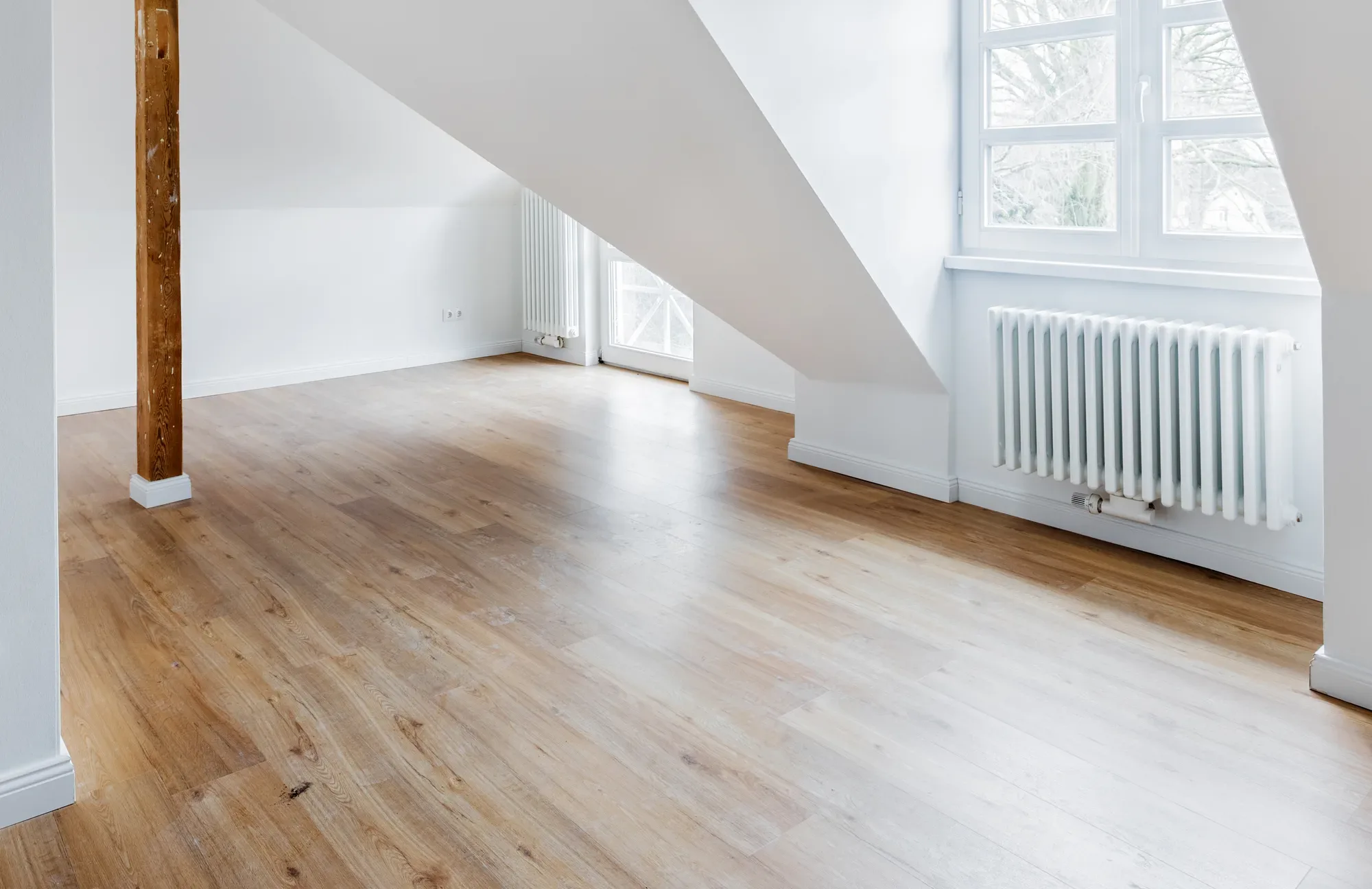 Lege, bezemschoon opgeleverde kamer met houten vloer en radiator