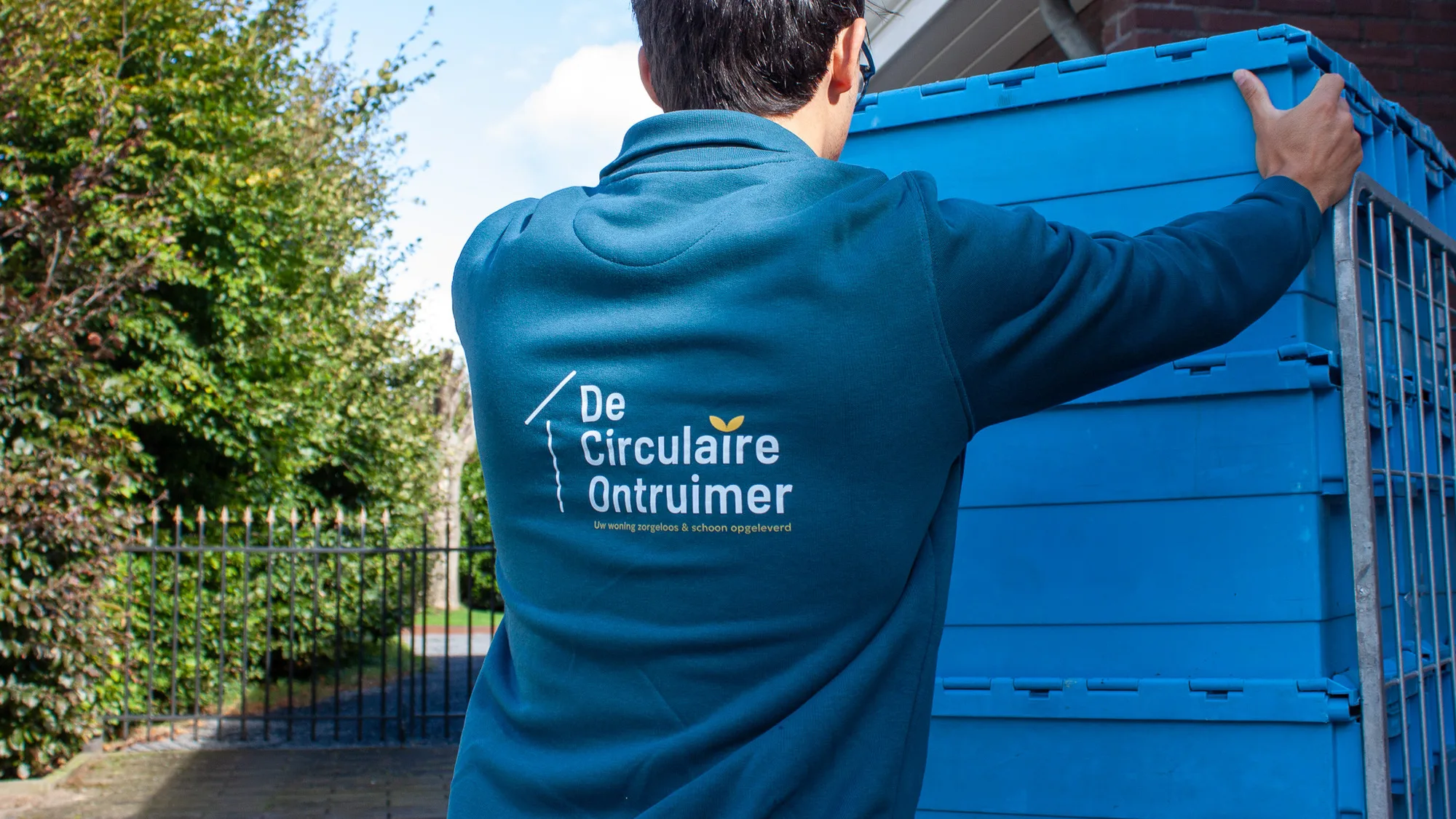 Medewerker van De Circulaire Ontruimer tilt een opslagcontainer bij een woning