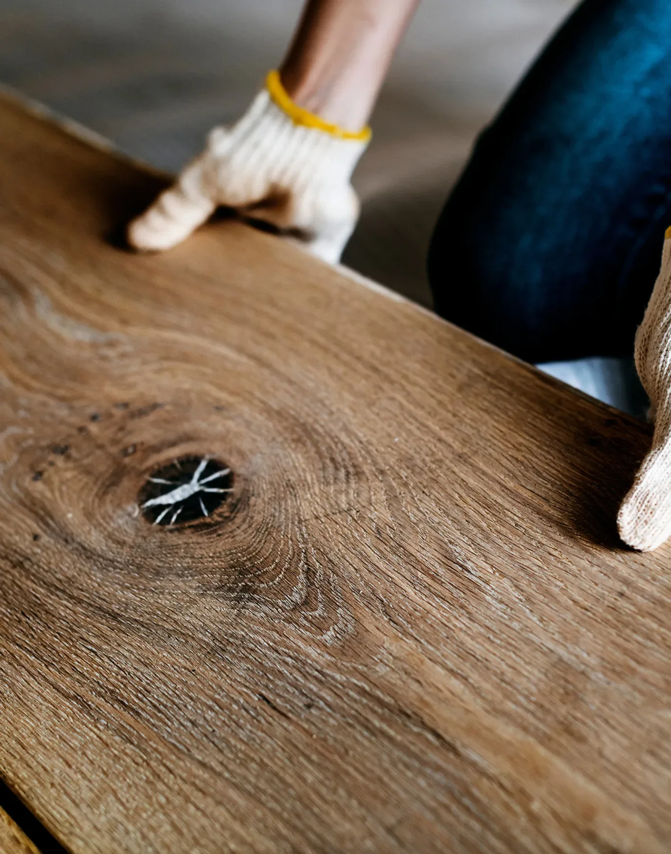 Handen met werkhandschoenen houden een houten vloerplank vast